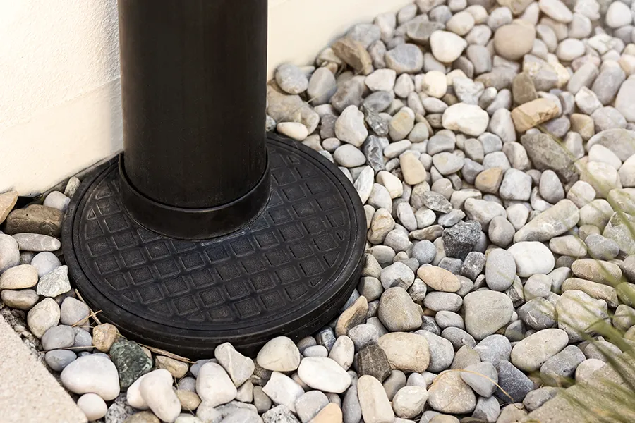 A close-up of a drainage downspout sitting in a decorative rock bed, showing proper grading and water-management design. - TaylorMade Landworks