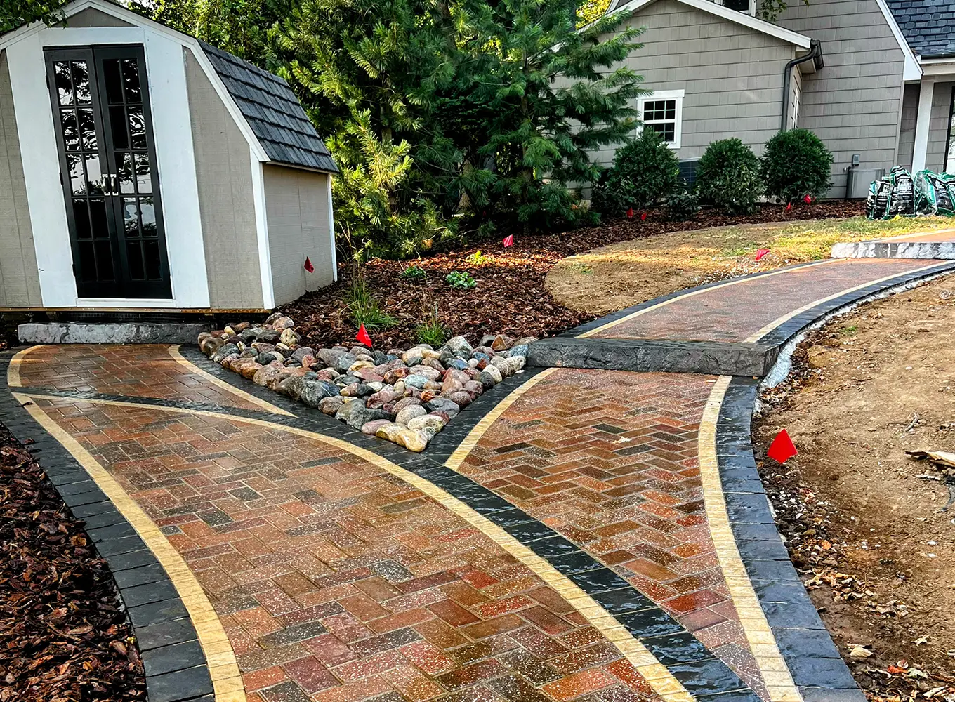 A custom brick walkway with decorative stone borders and a rock drainage feature leading to a shed, installed by TaylorMade Landworks in Springfield, IL.