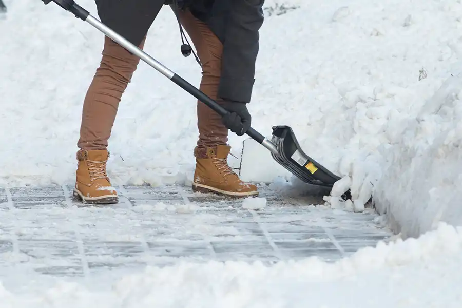 Taylormade Landworks—A worker in boots shovels a walkway during the winter months in Springfield, IL.
